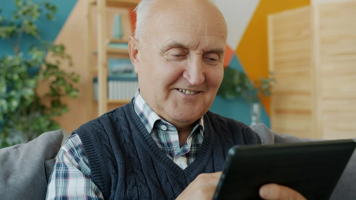 Älterer Mann bedient ein Tablet auf dem Sofa