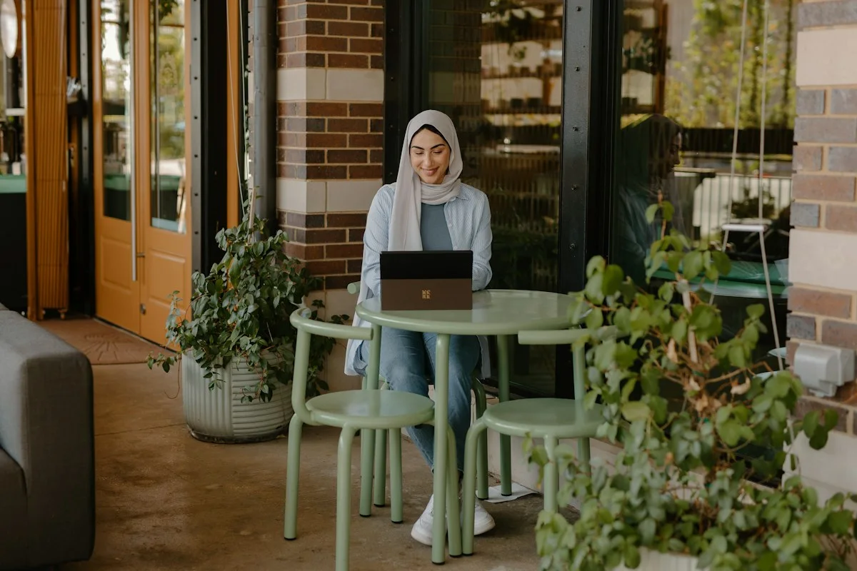 Eine Frau sitzt mit einem geöffneten Notebook an einem Tisch.